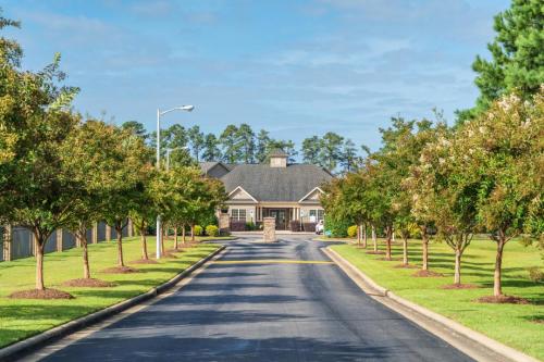 Apartments in Fayetteville, North Carolina Driveway lined with trees leads to a house with a gray roof, surrounded by greenery and a clear blue sky. Parcstone Apartments For Rent in Fayetteville