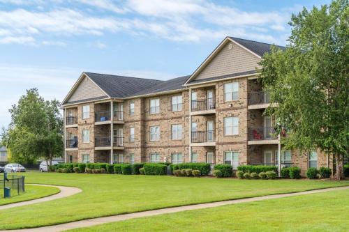 Apartments in Fayetteville, North Carolina Three-story brick apartment building with balconies, surrounded by well-maintained grass and trees under a clear blue sky. Parcstone Apartments For Rent in Fayetteville