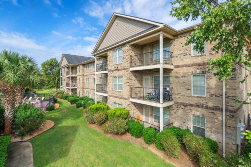 Apartments in Fayetteville, North Carolina A three-story brick apartment building with balconies, surrounded by trees and shrubs, under a blue sky. Parcstone Apartments For Rent in Fayetteville