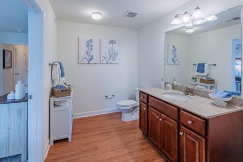 Apartments in Fayetteville, North Carolina Modern bathroom with wooden flooring, a large mirror above a granite countertop, dual sinks, decorative wall art, and soft lighting. Parcstone Apartments For Rent in Fayetteville