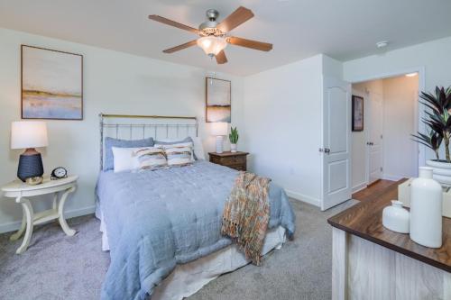 Apartments in Fayetteville, North Carolina A cozy bedroom with a neatly made bed, soft blue bedding, a ceiling fan, and minimal decor. Two bedside tables with lamps and a wooden dresser are visible. Parcstone Apartments For Rent in Fayetteville