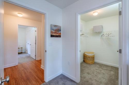 Apartments in Fayetteville, North Carolina Hallway with wooden floor leads to a room on the left and a carpeted walk-in closet on the right, featuring wire shelves, hangers, and a wicker laundry basket. Parcstone Apartments For Rent in Fayetteville